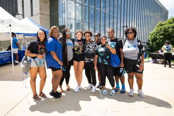 group of students and one staff member stand for a photo on courtyard near Pew Library