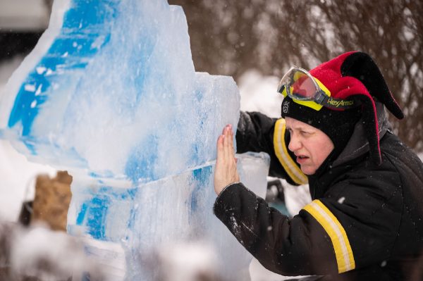 A person leans against an ice carving of Michigan and the Great Lakes during Winterfest on the GVSU Allendale Campus 