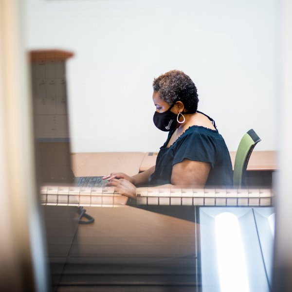Tiana Hawver answers a call on her computer in her office, she is wearing a mask.
