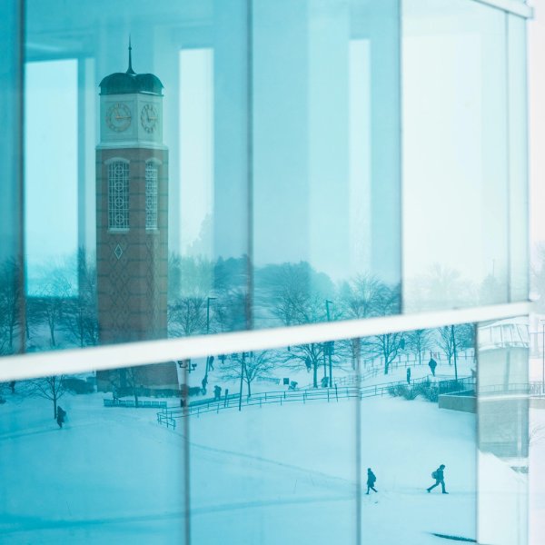 the Cook Carillon Tower is pictured in Zumberge Hall windows, along with people walking on the sidewalks