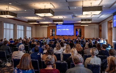 View from the back of a crowded room showing seated audience members facing the GVSU Board of Trustees.