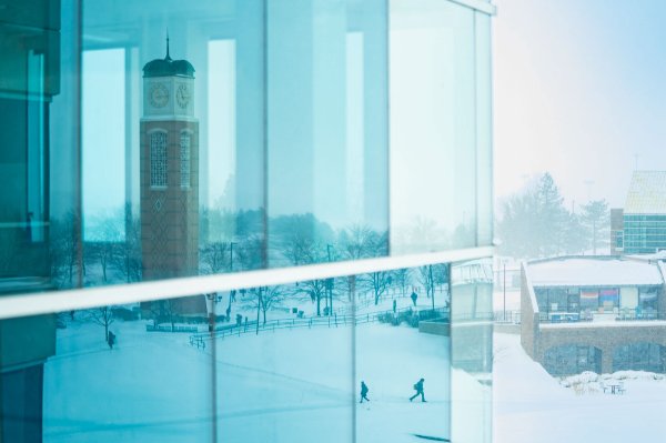 A reflection of students walking on a snow-covered college campus.