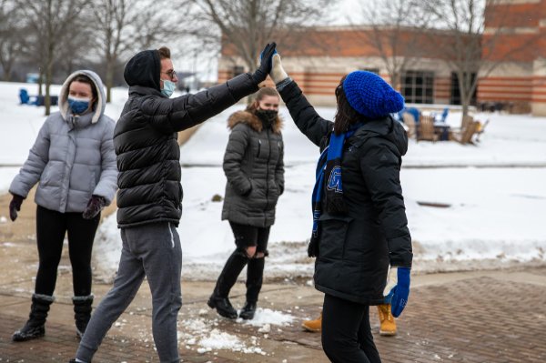 A college student high fives a university president on a wintery campus.