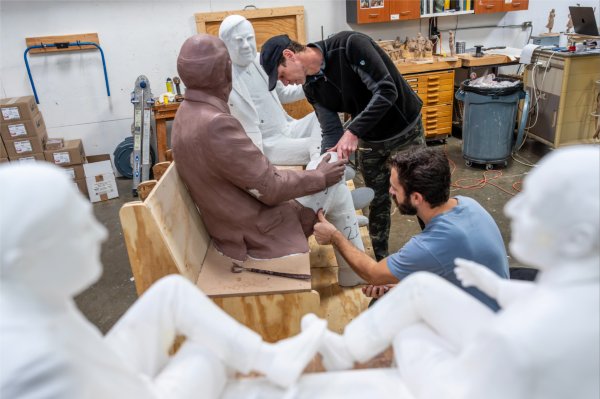 Two people are working on a sculpture in progress. Some parts are in styrofoam, while others are in clay. They are in an art studio.