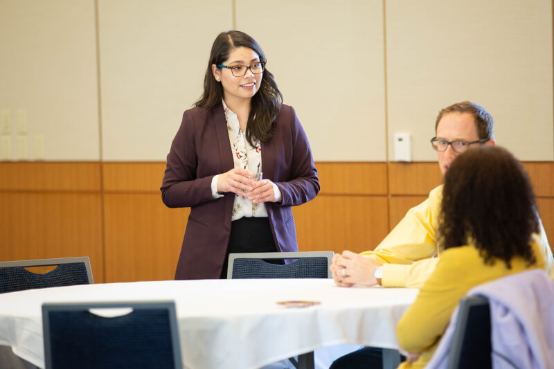 woman standing talking to 2 people at a table