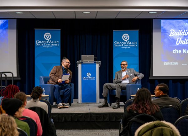 Robert Shorty, left, and Derrick Johnson seated on stage, GVSU banners behind them