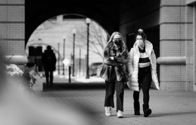 two students wearing masks walking near the Student Services Building, arch in background