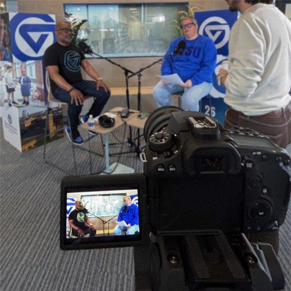 B. Donta Truss, left, and Michelle Rhodes seated in chairs for a podcast episode, a camera recording in front