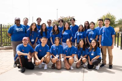 three rows of people standing in blue t-shirts outside the Mary Idema Pew Library