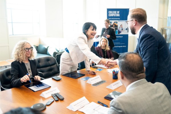 President Mantella stands to shake hands with Henry Ford College President David M. Knezek; a GVSU College of Computing vertical banner is in the background