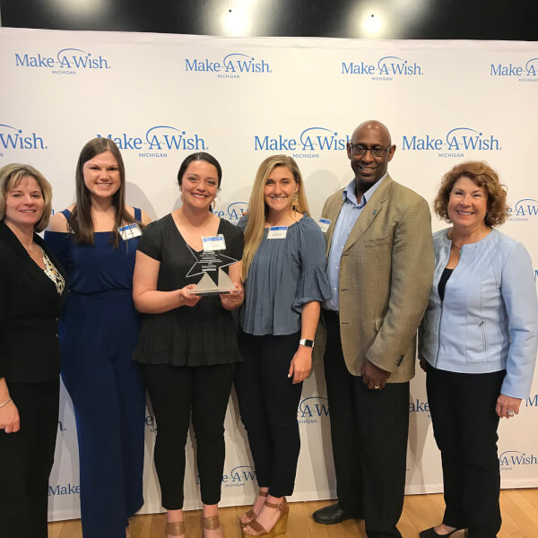 six people standing in front of Make-A-Wish Michigan backdrop
