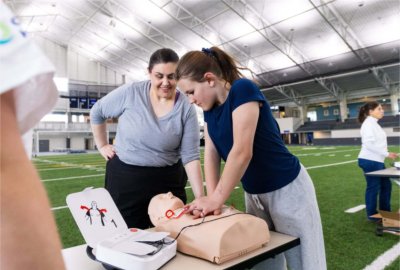A person practices CPR on a manikin while another looks on.