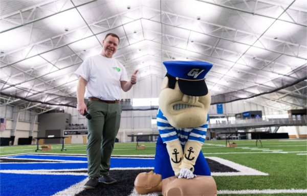 Louie practices CPR on a manikin while another person looks on.