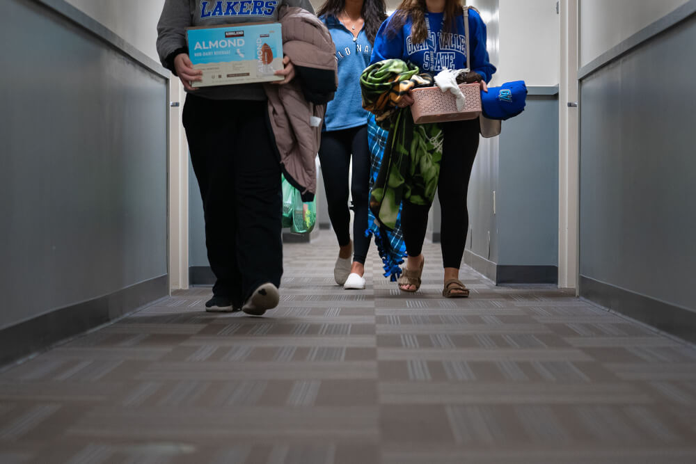 Three students holding stuff walking down a living center hallway.