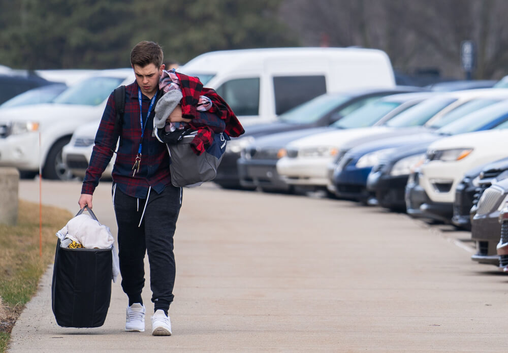 male student carrying belongings in parking lot