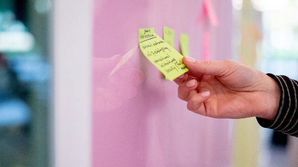 A close-up of a hand placing a yellow sticky note on a whiteboard. 