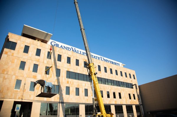 crane begins to hoist sculpture to rooftop of DCIH building, clear blue sky, no clouds