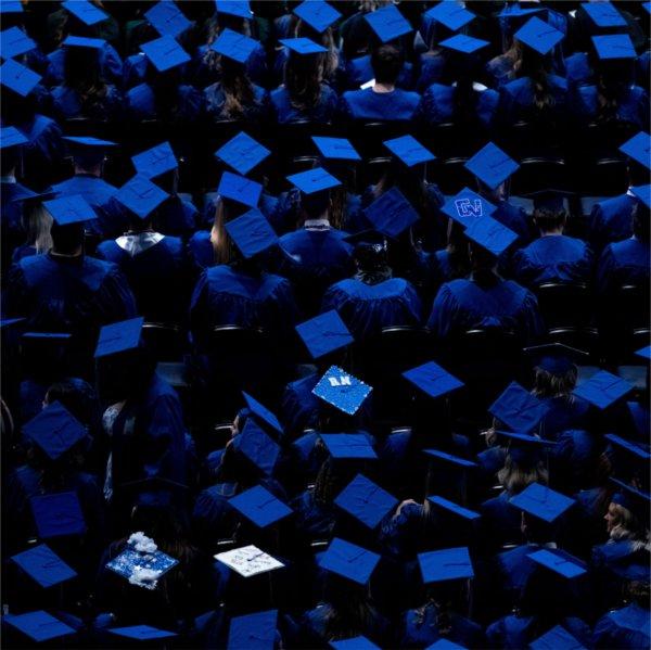Seen from above, graduates wearing blue caps and gowns are seated in anticipation for Commencement.
