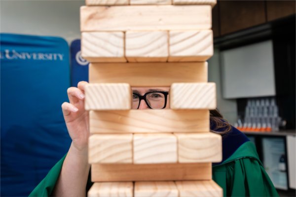 A person wearing glasses can be seen through a gap in a large Jenga game. 