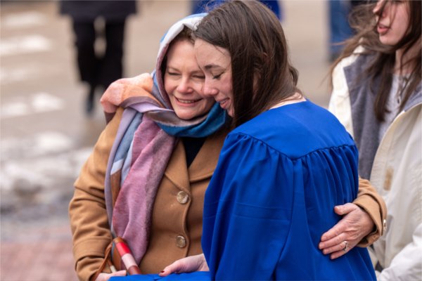  A mother and daughter embrace as the daughter, wearing a blue cap and gown, prepares for Commencement. 