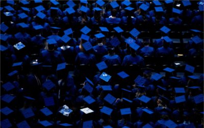  Seen from above, graduates wearing blue caps and gowns are seated in anticipation for Commencement. 