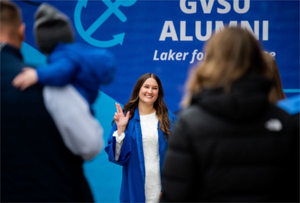  A graduate wearing a blue gown holds up an Anchor Up hand sign. 