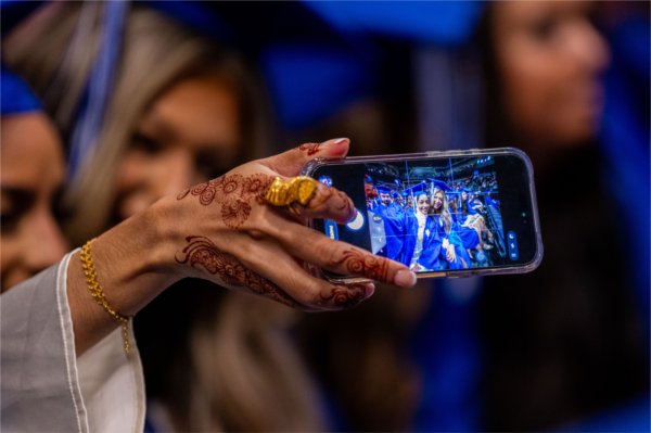  A hand adorned with henna takes a selfie with a cellphone. 