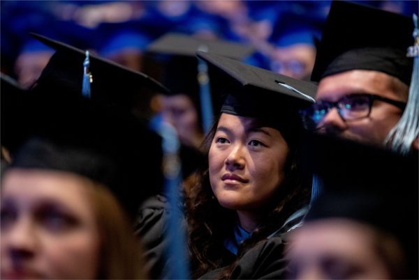  Graduates looking proud as they sit in caps and gowns and listen to Commencement speakers. 