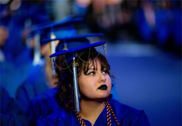  A graduate wearing a blue cap and gown with adornments listens to Commencement speeches. 
