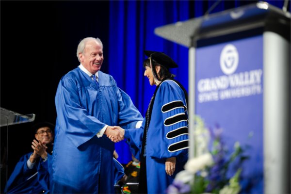  A man wearing a graduation gown shakes hands with a university president wearing academic regalia. 