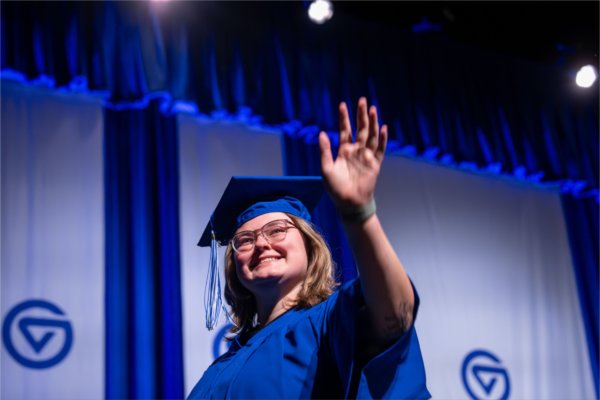  A graduate wearing a blue cap and gown waves. 