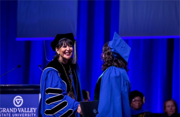  A university president in academic regalia shakes the hand of a graduate in a cap and gown. 