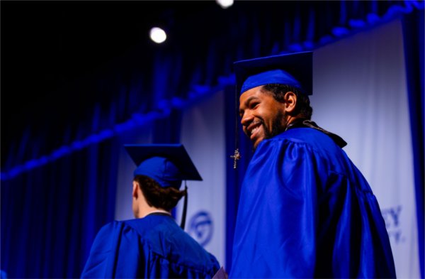  A graduate wearing a blue cap and gown smiles as they cross the stage.