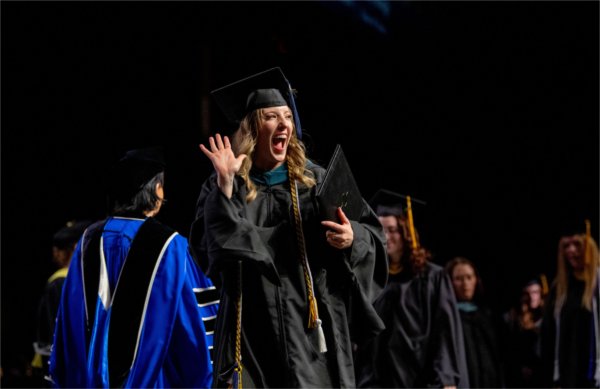  A graduate wearing a blue cap and gown waves. 