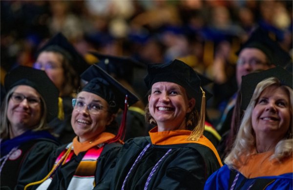  A group of smiling faculty members wearing academic regalia sit during Commencement. 
