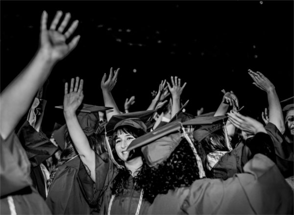  Graduates wearing caps and gowns wave to their family and loved ones in the audience.  