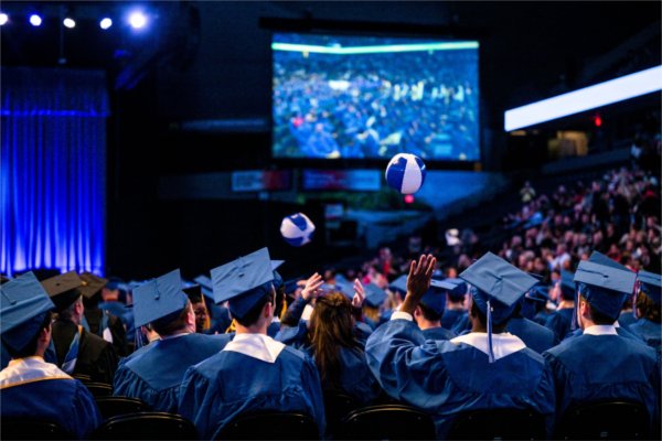  Graduates in blue robes and hats pass small beachballs in the air.
