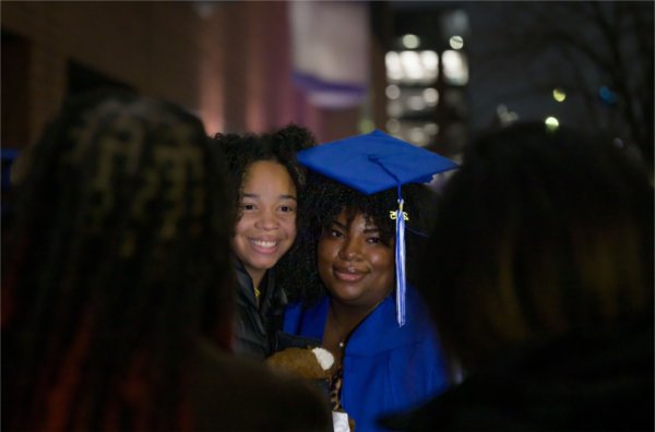 A graduate in a blue cap and gown poses next to a smiling person.