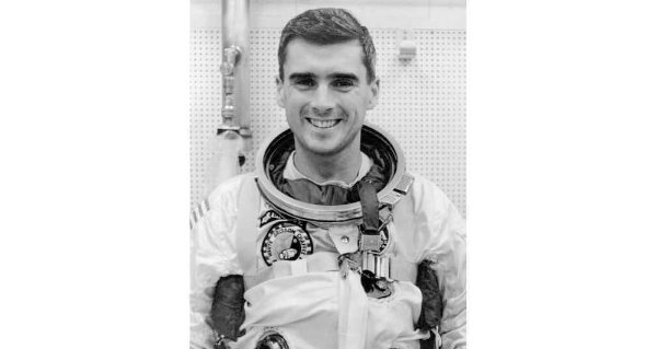 A person wearing an astronaut uniform smiles in a black and white photo.