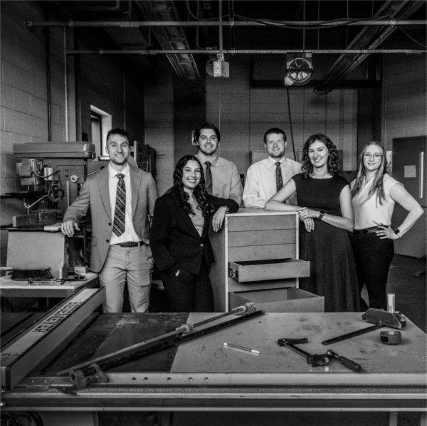 six students stand behind a cabinet in a woodshop
