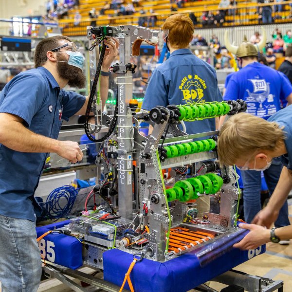 several high school students in blue team shirts work on a robot at the Fieldhouse during the FIRST Robotics competition