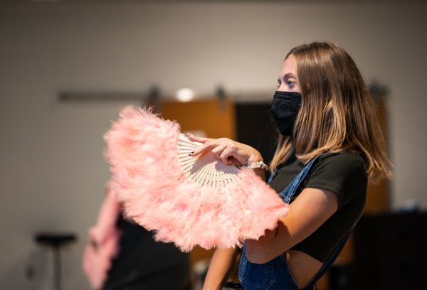 A performer holds a pink-feathered fan while rehearsing.