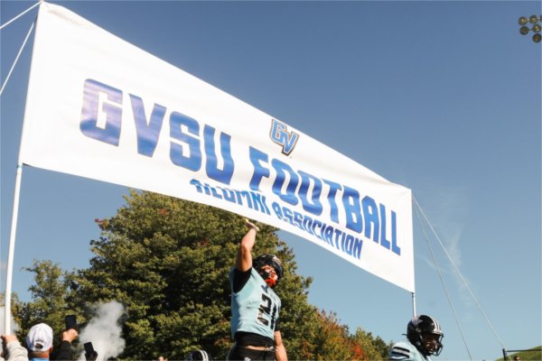 A GVSU Football player jumps to touch the 'GVSU Football' banner at the start of the Homecoming game on October 3.