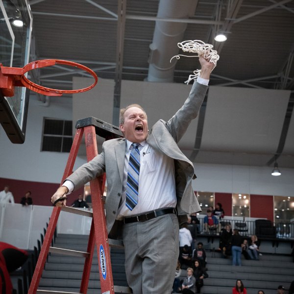 Head men's basketball coach Ric Weasler celebrates a victory after cutting down a basketball net