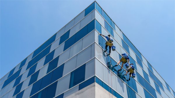 Three window washers in harnesses clean the tall glass windows of Zumberge Hall.