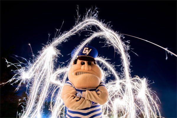 Louie the Laker stands with his arms crossed as bright sparklers swirl in the night sky behind him.