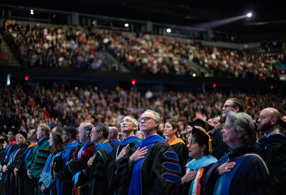 crowd of faculty standing at commencement in audience
