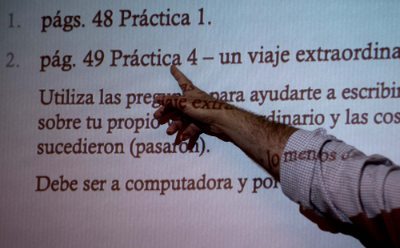 a hand points to words in Spanish projected on a screen