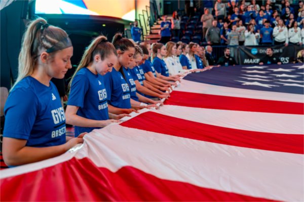 Members of the Grand Valley women's basketball team bow their heads while collectively holding a large American flag.