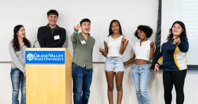 High school students stand behind a podium gesturing while giving a presentation.